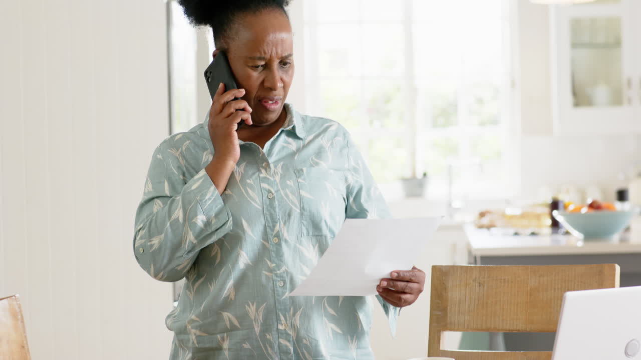 African american senior woman doing paperwork and using smartphone in sunny room, slow motion