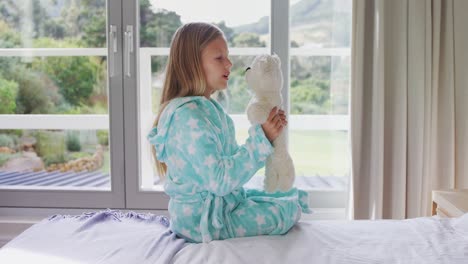 chica jugando con un oso de peluche en la cama 4k