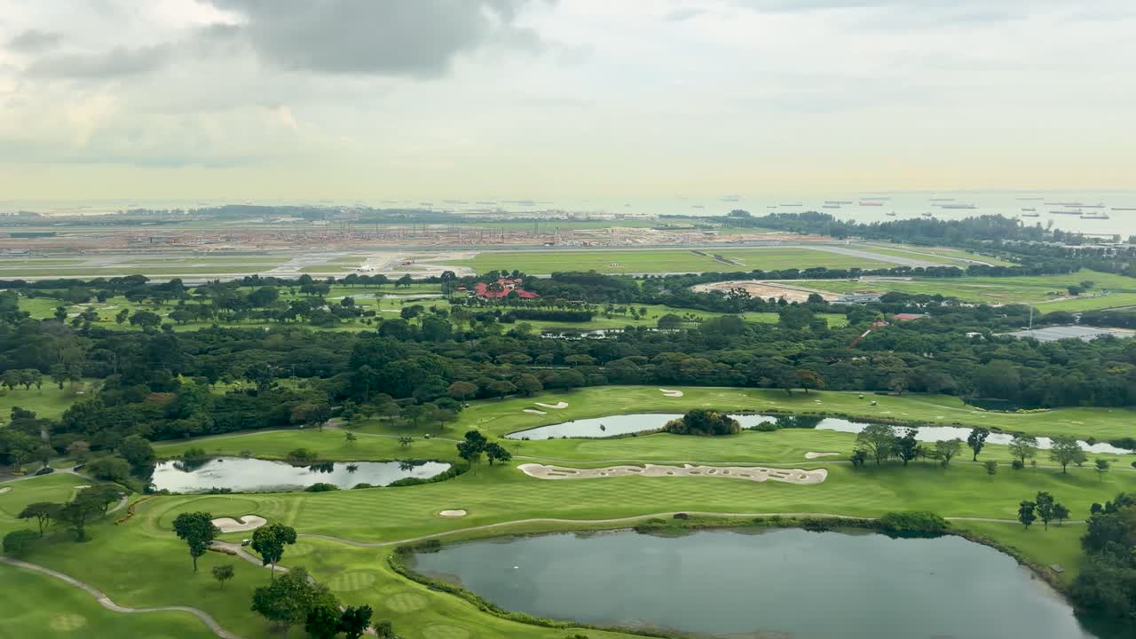 Smooth aerial flyover of green golf course with ponds, bunkers, coastline, and overcast sky