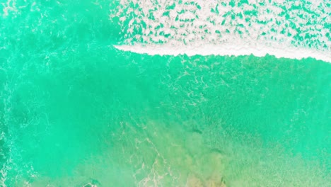 areal top view shoot of waves closing to coastline, crystal clear sea water and rocks visible in shallow surface