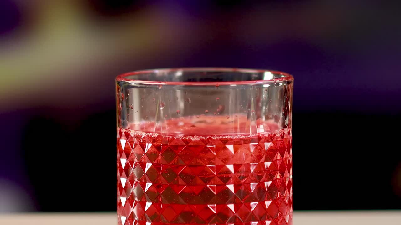 Red liquid pours into a textured glass against a colorful background, creating a vibrant and dynamic scene