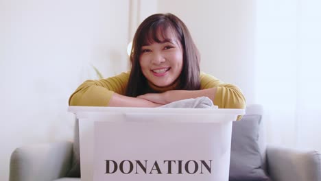 portrait of young asian woman looking at camera holding box with clothes for donation