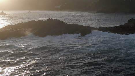 Ocean-waves-splash-onto-rocks,-backlit-by-ethereal-golden-sunlight