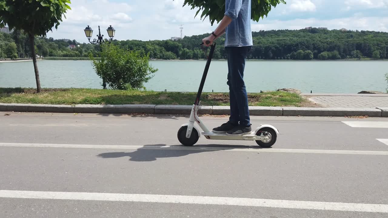 CHISINAU, MOLDOVA - 9. juli 2019: Mand, der kører på en hvid, elektrisk scooter i Valea Morilor-parken. Sø i baggrunden