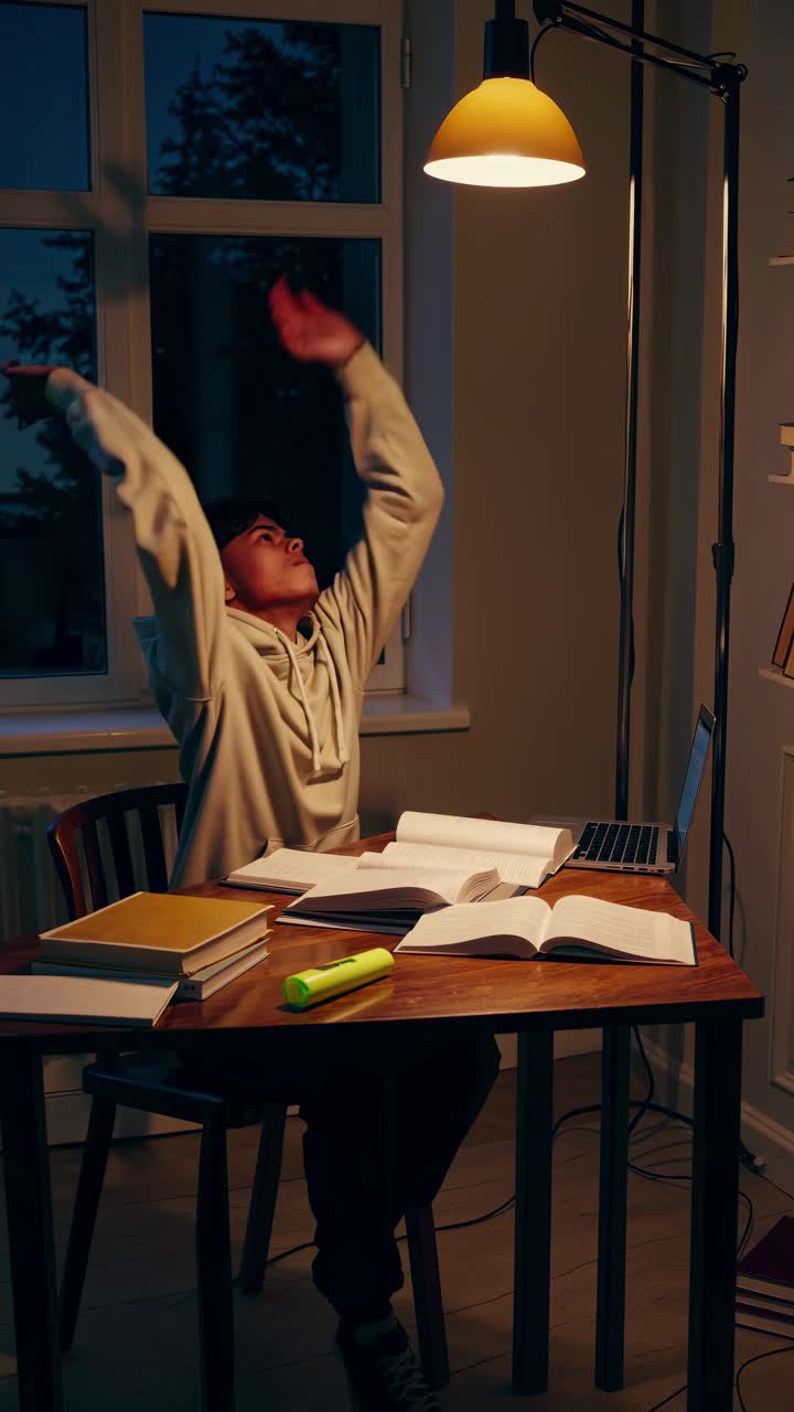 A moody, low-angle shot of a person studying at a desk, illuminated by a warm lamp
