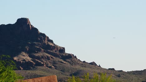 desert mountain landscape with a distant airplane flying behind the rocky ridge under a clear sky
