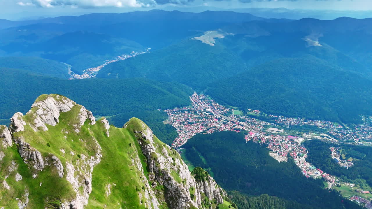 Aerial view of Bucegi Mountains and mountain town. Aerial scenic view of Bucegi Mountains cliffs and a mountain town surrounded by forests
