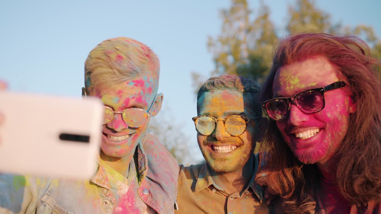 Slow motion of cheerful guys multi-ethnic friends taking selfie at Holi festival