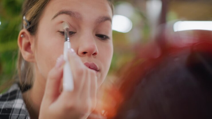 Close-up view of lady adjusting makeup on her eyes using a brush while reflecting in a blurred mirror, she carefully applies makeup for a polished and flawless look