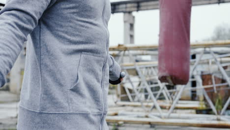 close-up view of caucasian man with a beard in a grey hoodie jumping rope outdoors an abandoned factory on a cloudy morning