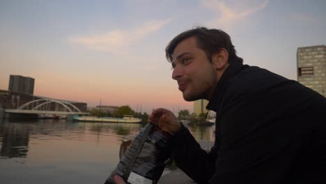 close up of a young man eating potato chips out of bag suring sunset on a waterfront pier