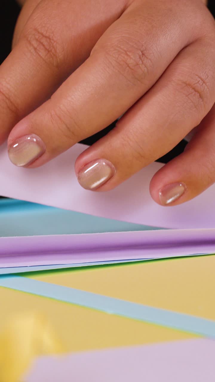 Close up shot of fingers folding purple paper over blue and yellow sheets on black