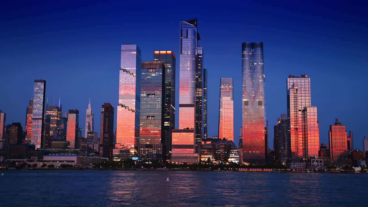 Nova York, EUA, 8 de julho de 2025: impressionantes edifícios altos refletem a luz rosa do pôr do sol. Vista de baixo ângulo da arquitetura de Nova York a partir da margem do rio ao pôr do sol