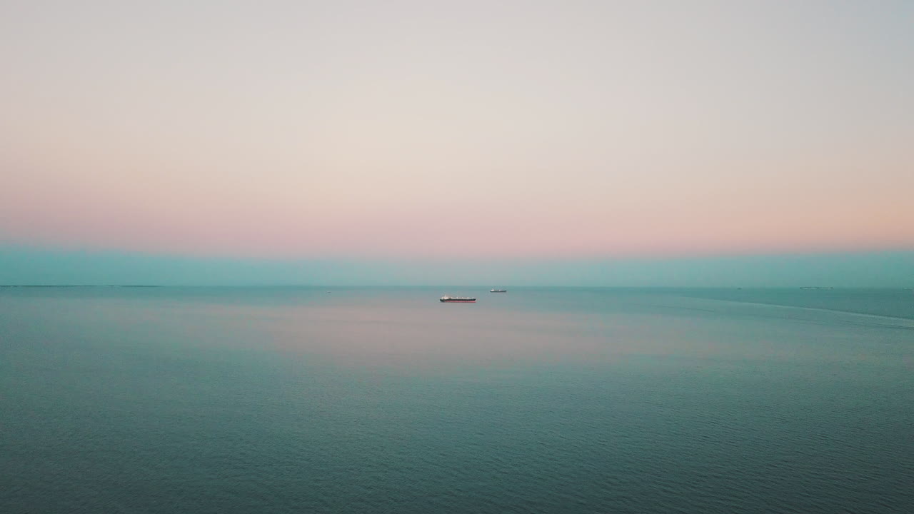 석양을 배경으로 화물선과 함께 바다 위를 날고 있는 드론