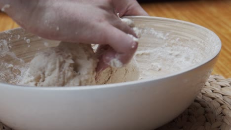 El-Chef-Moldea-La-Masa-De-Pizza-En-Un-Plato-Hondo,-Sobre-Una-Mesa-De-Madera