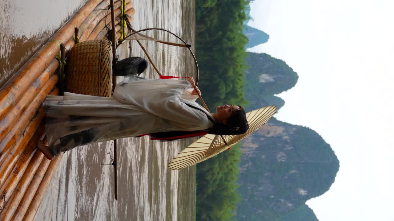 Ragazza in Hanfu con lanterna che osserva il paesaggio montuoso da una zattera sul fiume Li, Cina