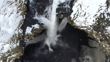 Antenne:-Nahaufnahme-Des-Wasserfalls-Im-Schnee,-Eisschlucht-In-Island,-Grünes-Gras,-Bewölkt