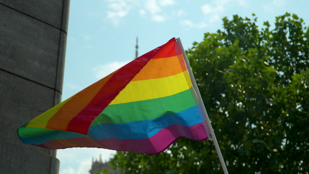 la bandera lgbt en un poste blanco ondea en el viento, con una sección del palacio de la cultura en el fondo - marcha por la igualdad en varsovia en junio de 2023
