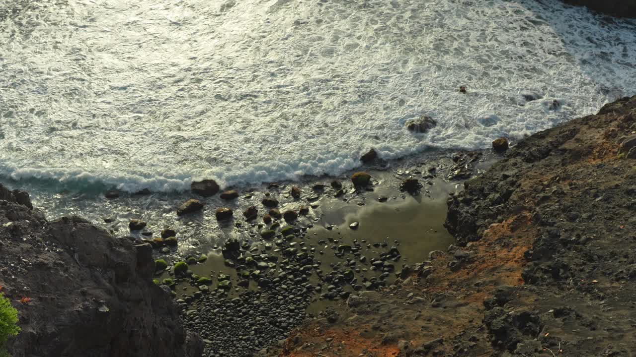 Wave crashes on Tenerife's rocky beach with volcanic black sand