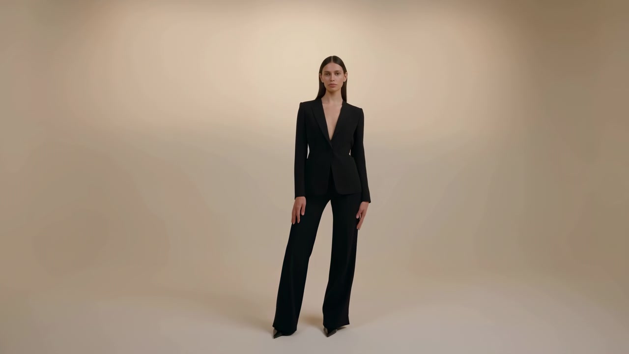 Tampilan seluruh tubuh menunjukkan seorang wanita mempertahankan pose tegak yang tenang sambil membuat perubahan kecil pada posisi tangan dan kaki, mengenakan setelan formal gelap dengan latar belakang mulus berwarna krem yang diterangi dengan lembut
