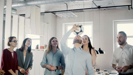 feliz trabajador caucásico haciendo malabarismos con el fútbol en la cabeza. alegres ejecutivos de raza mixta celebran el éxito comercial en la oficina 4k