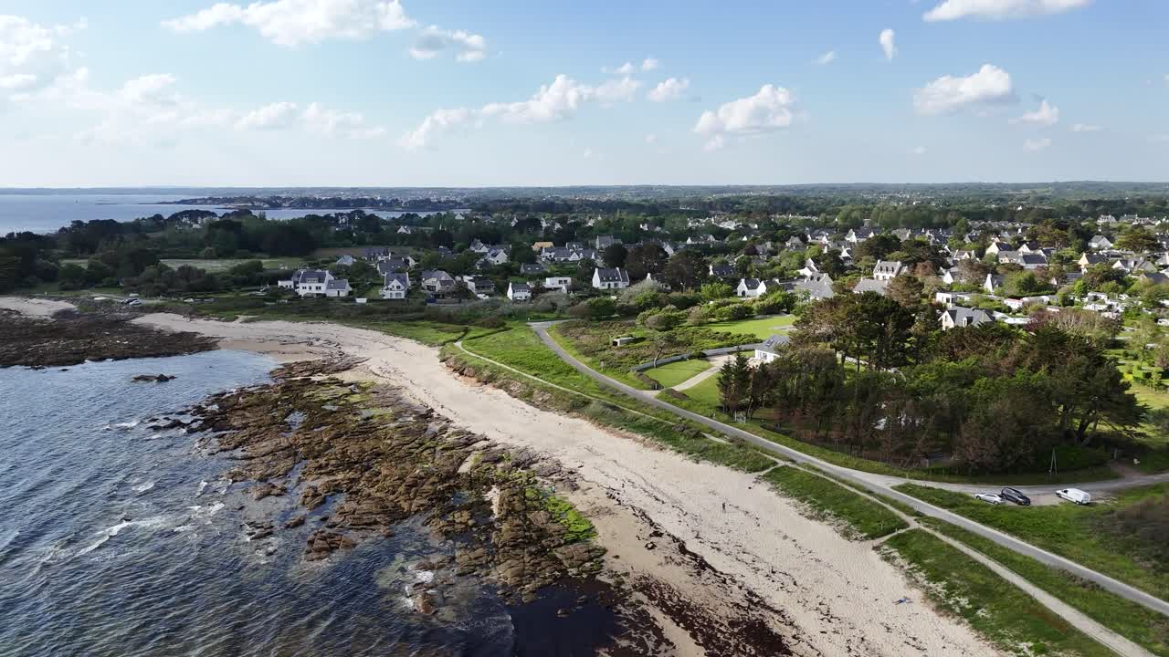 Vista aerea panoramica di un villaggio costiero con una spiaggia e case sotto un cielo azzurro limpido