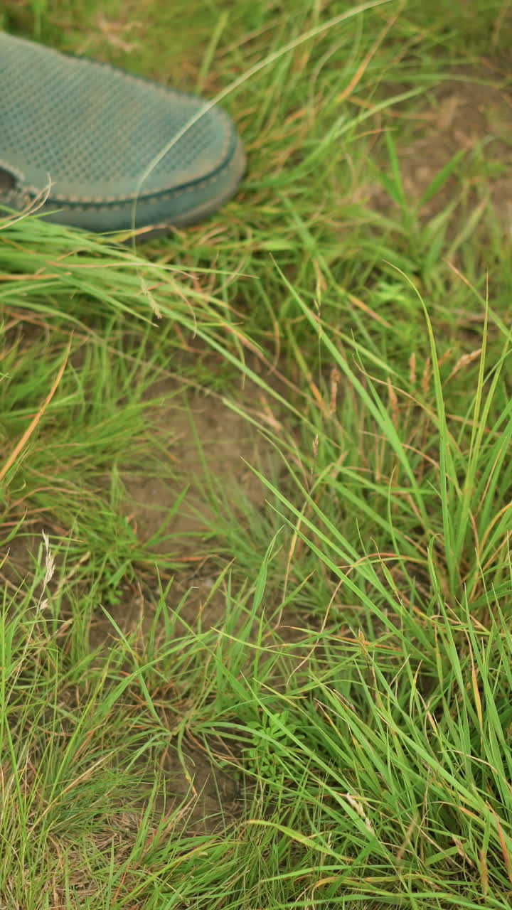un primer plano de un trípode de madera que se está estableciendo en un campo cubierto de hierba, con una pierna humana parcialmente visible, destacando la simplicidad y la practicidad de las actividades al aire libre