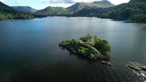 Orbit-of-small-island-in-dark-lake-with-slow-reveal-of-distant-mountains-on-bright-summer-day