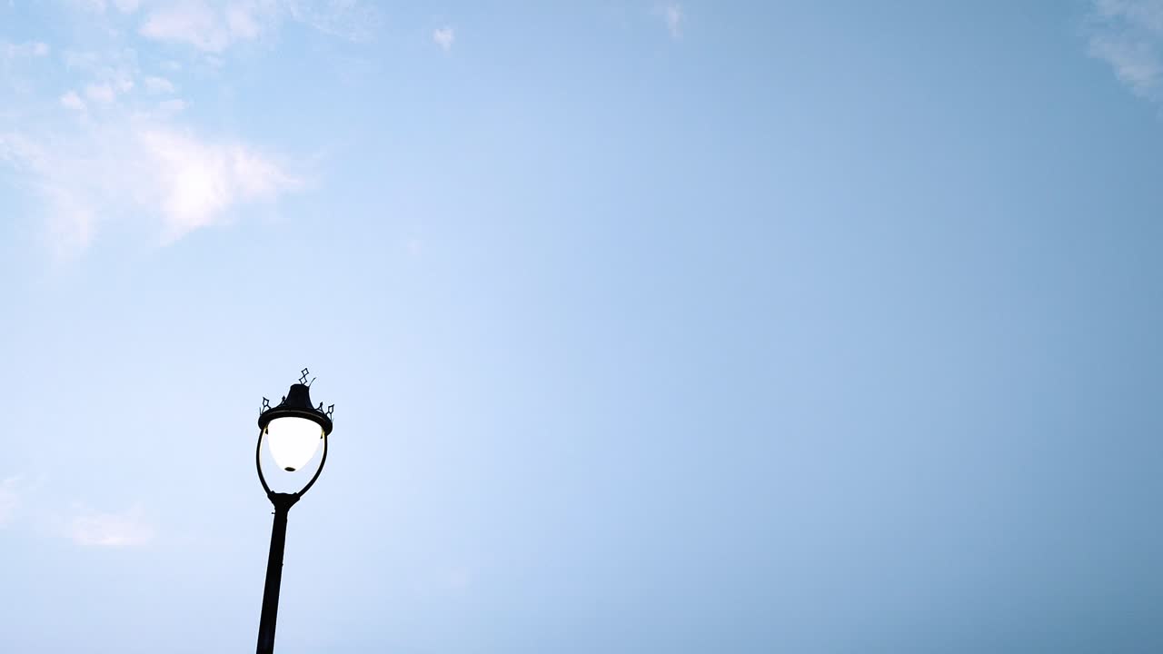 Real-time upward to downward tilt shot of vintage street lamp agains clear blue sky. Ideal for transitions, city scenes or background use in films and ads