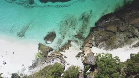 Birds-Eye-POV-over-sunny-beach-and-rocky-shore