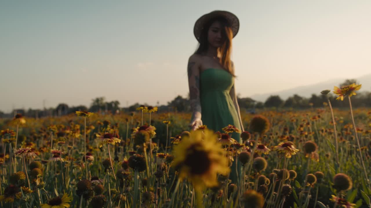 Woman in a green dress walking through a field of wildflowers at sunset
