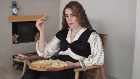 portrait depicts a young, beautiful woman in embroidered authentic ukrainian attire eating a cheese platter