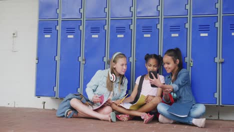 video de tres escolares felices y diversas mirando su teléfono inteligente, sentadas en el pasillo, en el espacio de copia