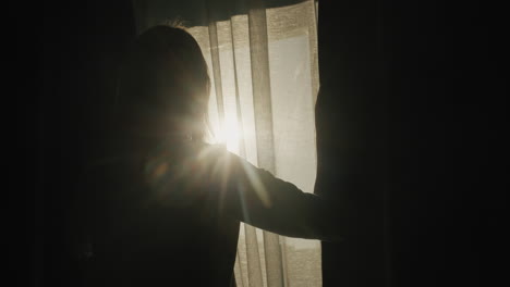 Silhouette-of-a-woman-who-opens-blackout-curtains.-It-is-illuminated-by-the-bright-sun-from-the-window