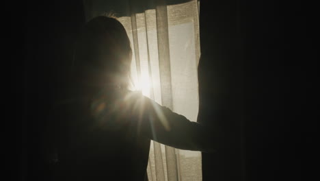 silhouette of a woman who opens blackout curtains. it is illuminated by the bright sun from the window