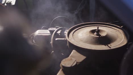 closeup of an old chevy pickup truck engine as it steams and fingers point to problem parts