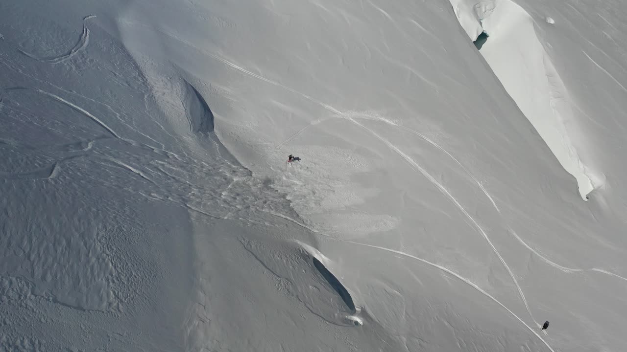 4K drone footage of snowboarder on steep slope with sluffing snow