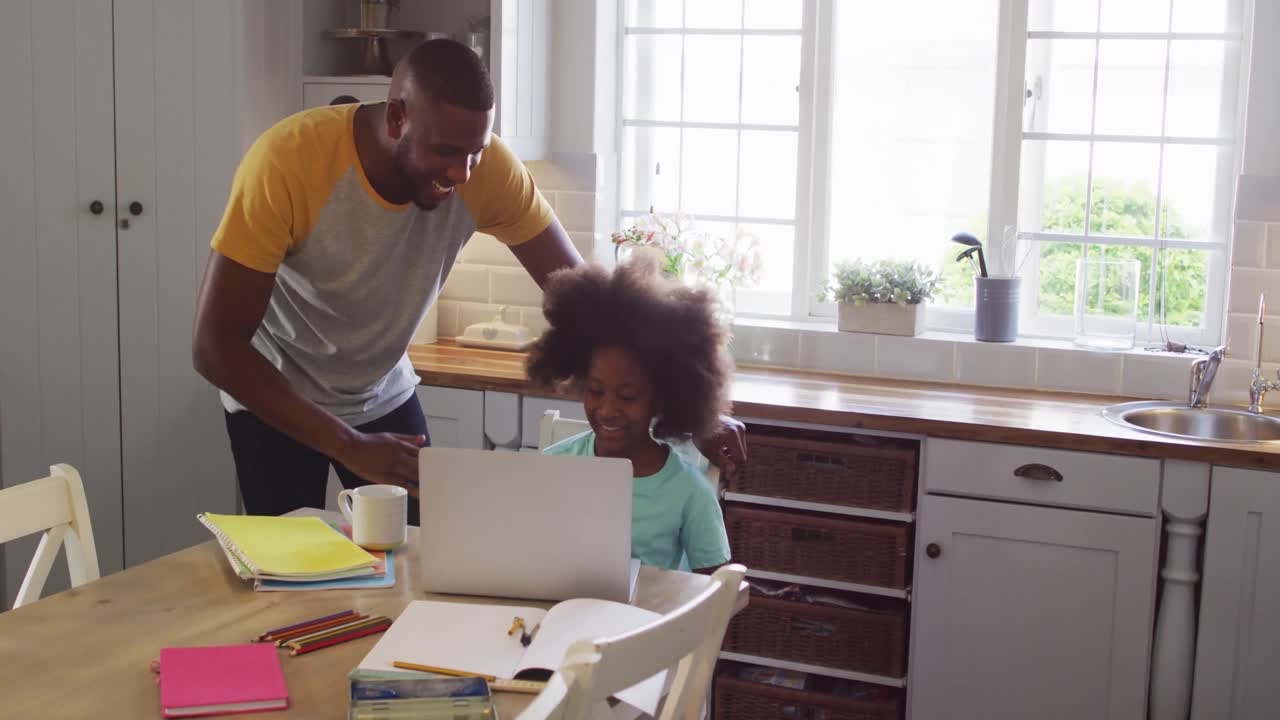African american daughter and her father using laptop together at kitchen table