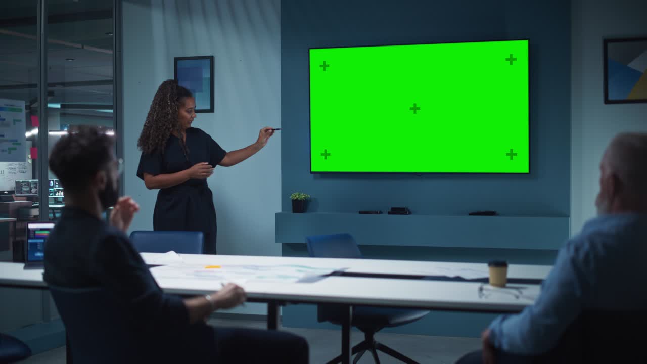 회사 운영 관리자는 임원 팀을 위해 회의 프레젠테이션을 개최합니다. 다민족 여성은 수평 녹색 화면 모의 디스플레이와 함께 넓은 tv 세트를 사용합니다. 사람들은 비즈니스 사무실에서 일합니다.