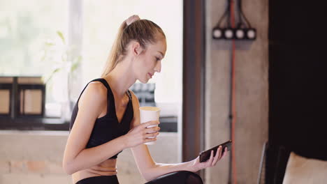 Lockdown-Shot-Of-Attractive-Young-Woman-Using-Smartphone-While-Relaxing-After-Workout-Session