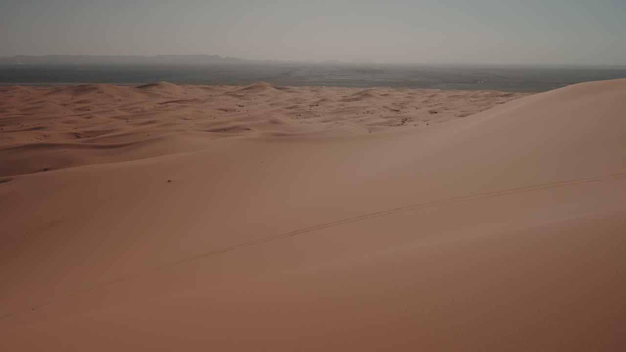 Vaste dune di sabbia arancioni che si estendono all'orizzonte sotto un cielo grigio e fosco nel deserto dell'Erg Chebbi