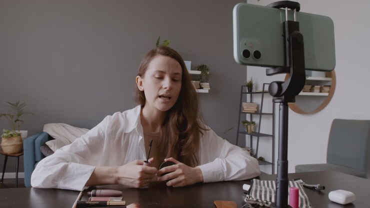 Giovane e bella vlogger che registra una recensione di un mascara davanti alla fotocamera del suo smartphone.