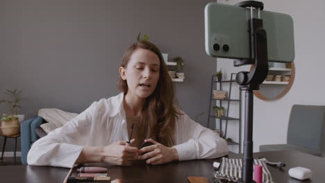 young beautiful vlogger female recording an eye mascara review in front of her smartphone camera