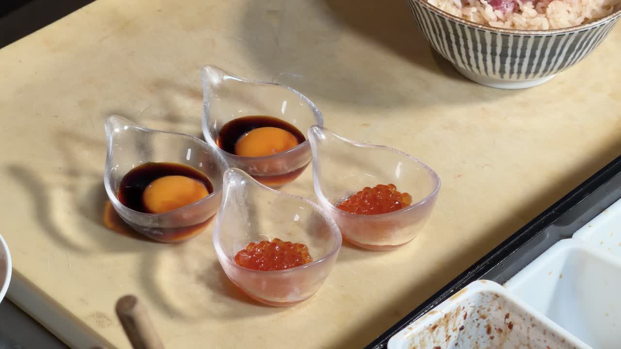 Overhead view of chef pouring dark ponzu sauce onto raw egg yolk and salmon roe