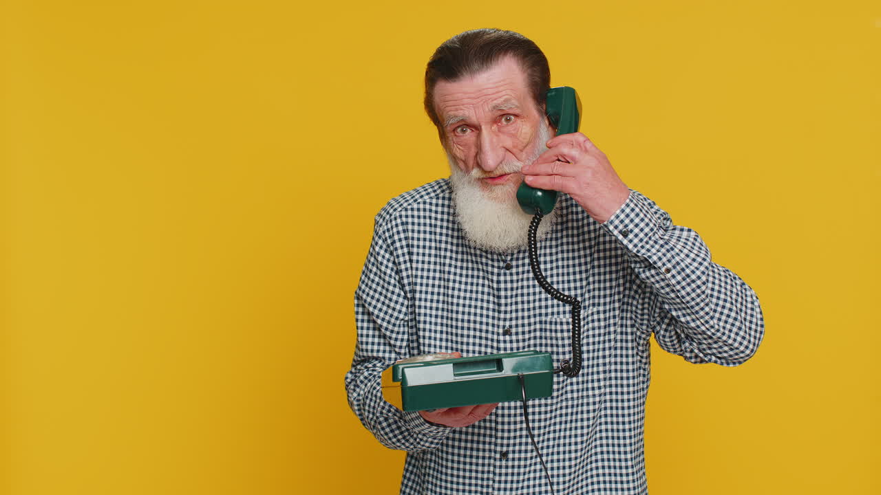 Senior man talking on wired landline vintage telephone advertising proposition of conversation