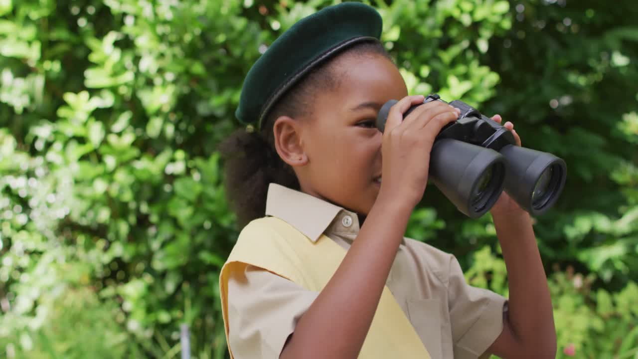 animación de una niña afroamericana en disfraz de explorador usando binoculares en el jardín