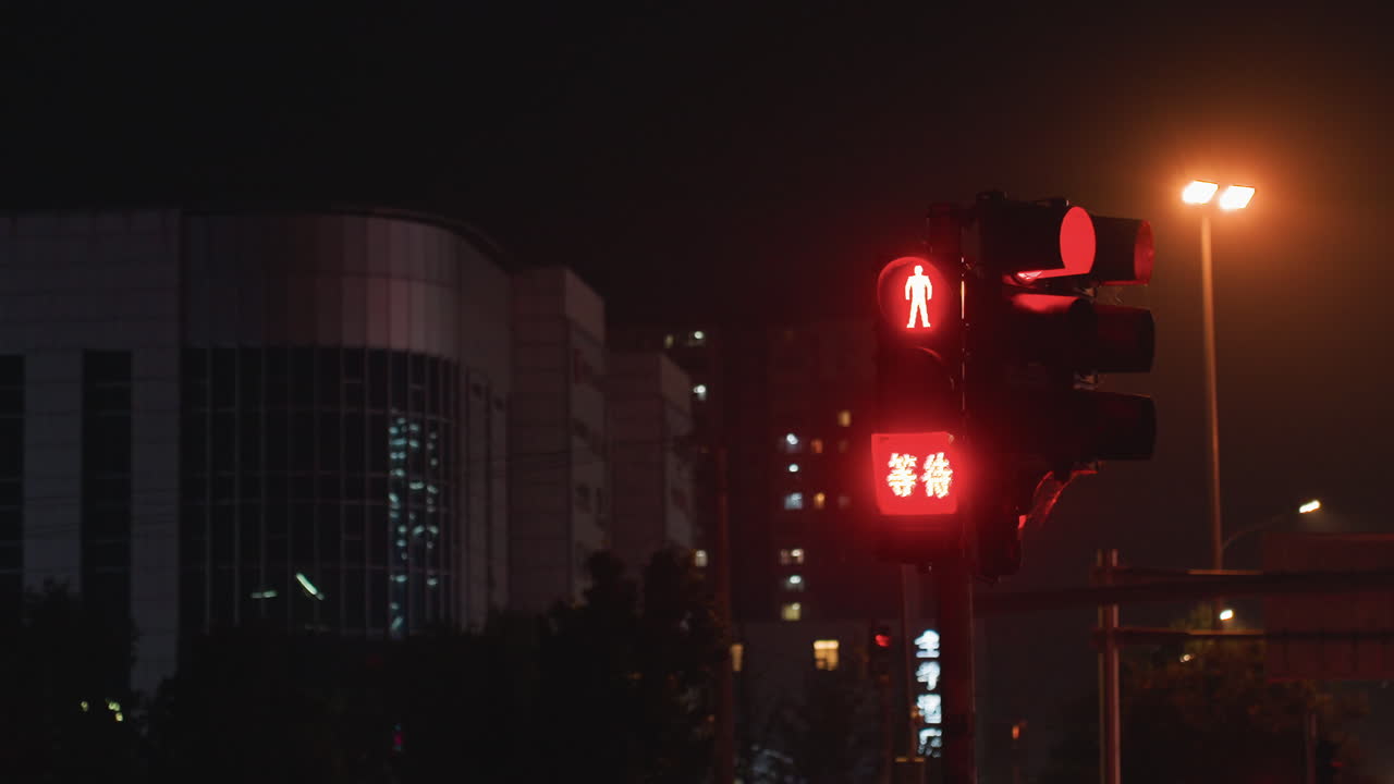 Semáforo de pedestres noturno alternando de vermelho para verde contra um cenário urbano nebuloso, display de contagem regressiva iluminado pulsa ao lado do brilho de um poste de rua e da silhueta de um edifício de escritórios moderno, criando quietude.