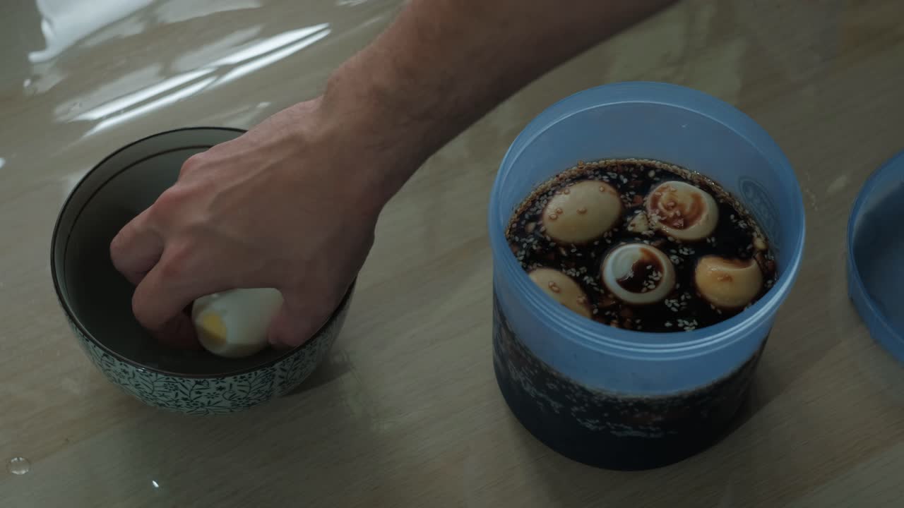 Placing hard-boiled eggs in a container full of soy sauce marinade and storing away. -static shot