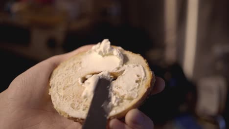 hands spreading butter on the homemade bagel for breakfast