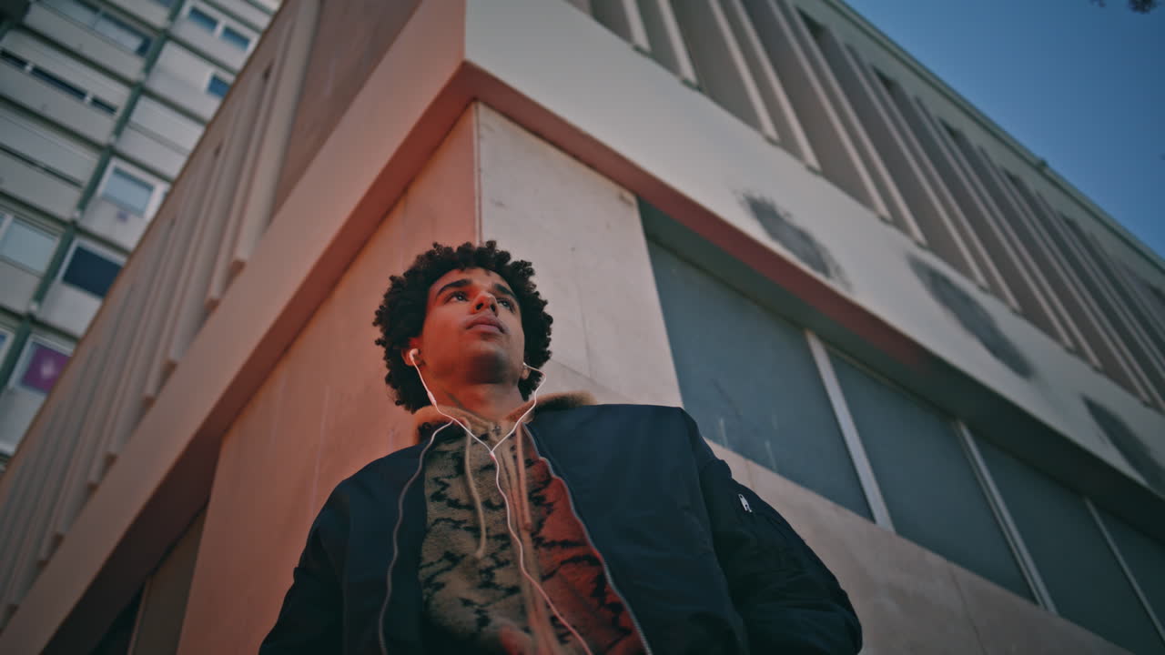 스타일리시한 남자가 청각기 음악을 듣고 부드러운 도시 저녁 빛에 둘러싸여 있습니다.